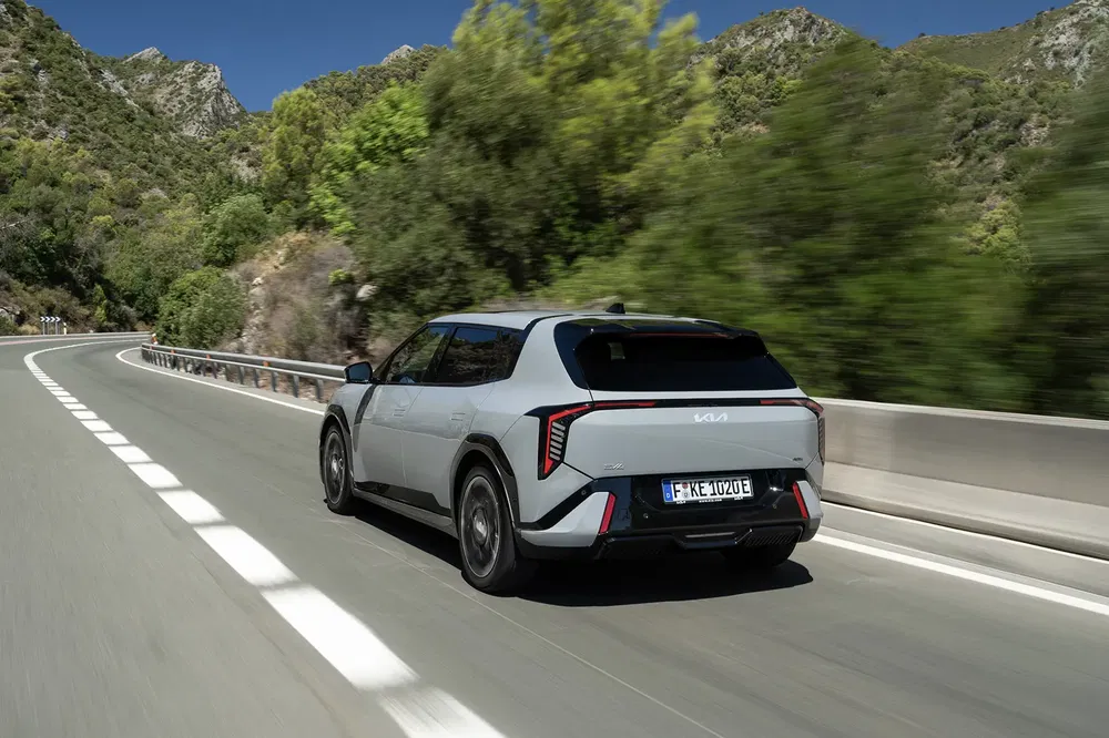 Kia EV9 roulant sur route sinueuse entourée de montagnes verdoyantes.