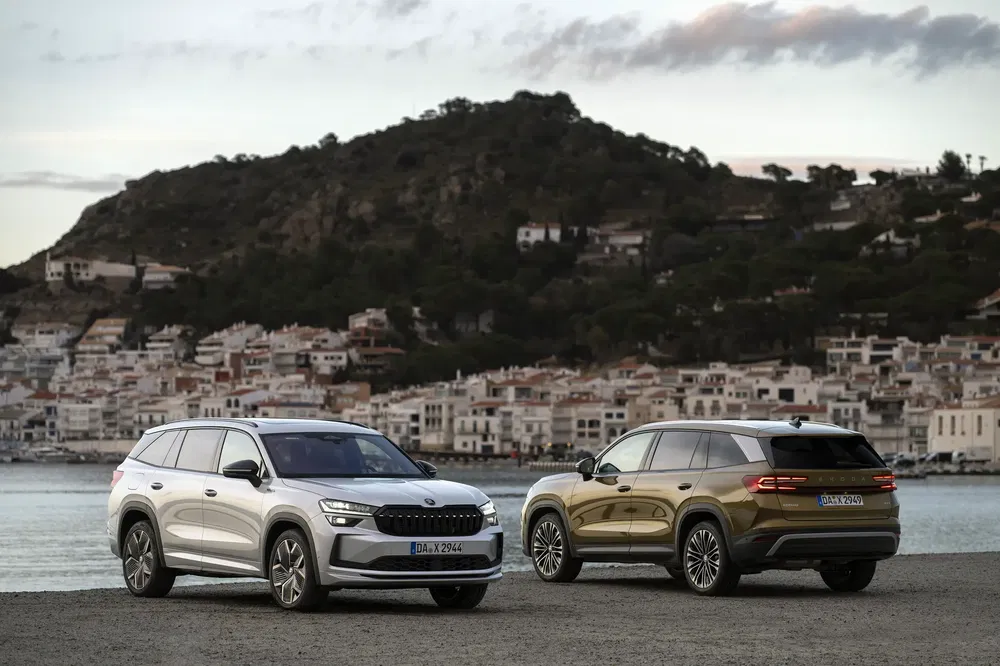 Twee Skoda Kodiak SUV's geparkeerd voor een schilderachtig bergachtig kustlandschap.