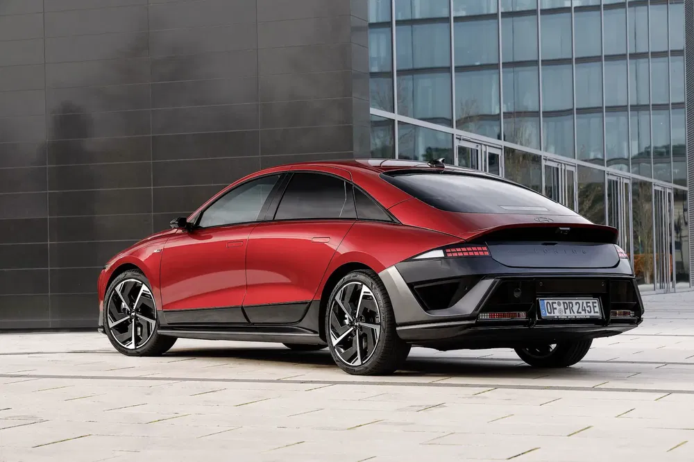 Hyundai Ioniq 6 rouge stationné devant un bâtiment moderne, vue arrière latérale.