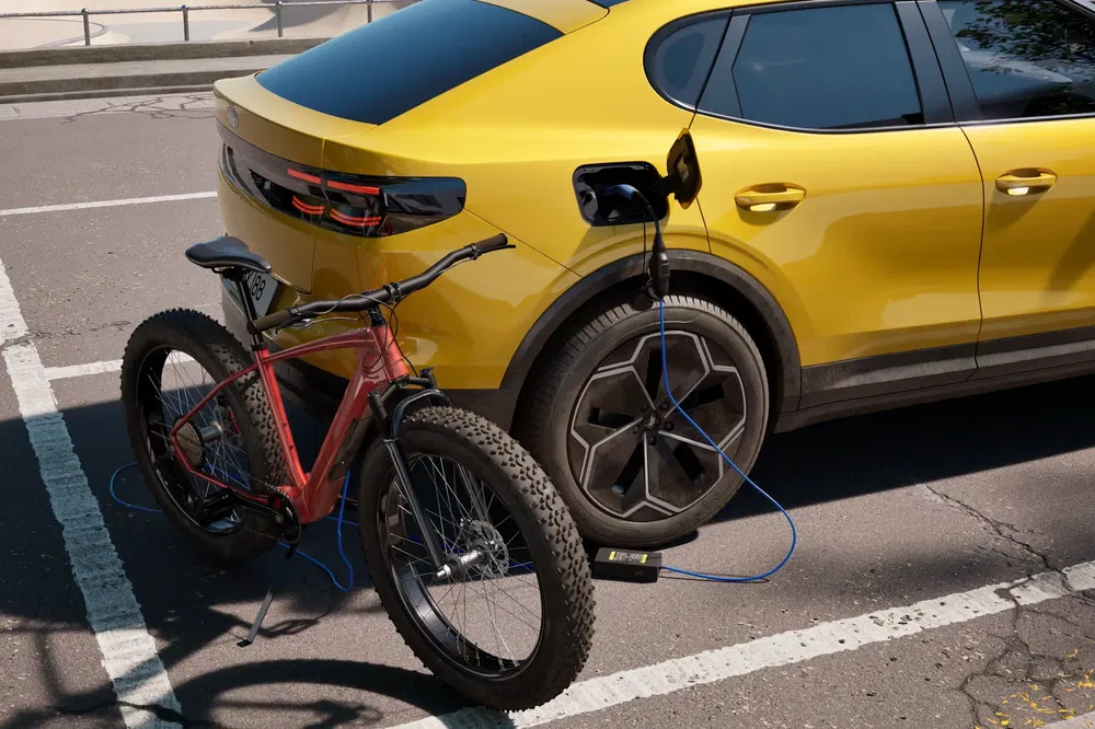Gele elektrische SUV laadt rode fiets op in stadsparkeerplaats.