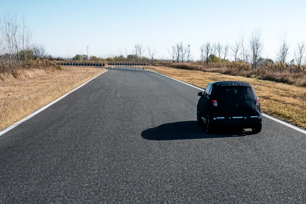 Voiture noire en essai sur piste asphaltée aride par journée ensoleillée.