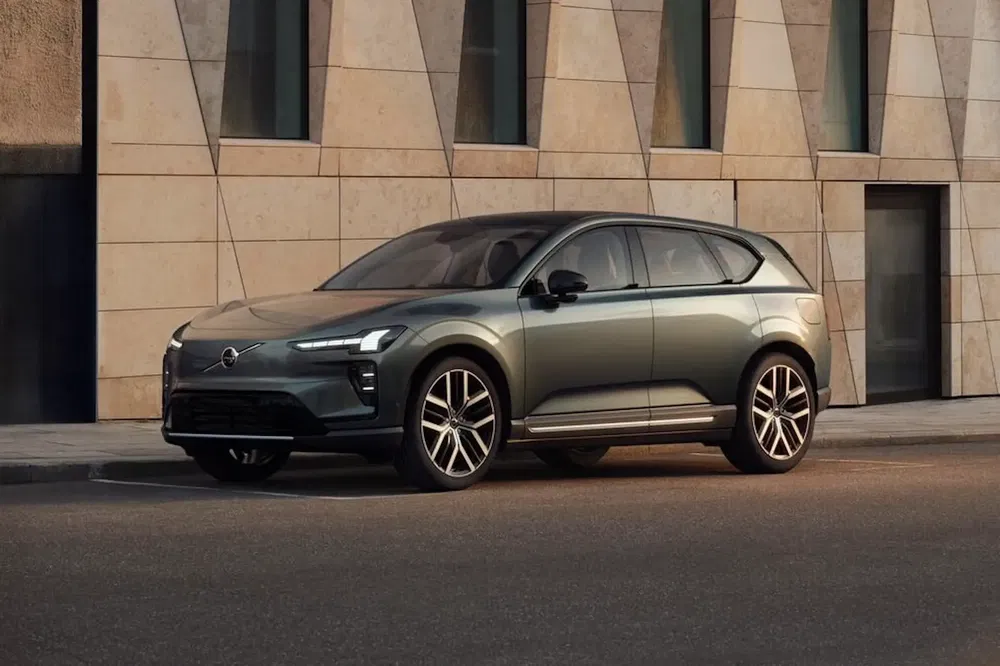 SUV électrique Volvo EX90 garé devant un bâtiment moderne en pierre.