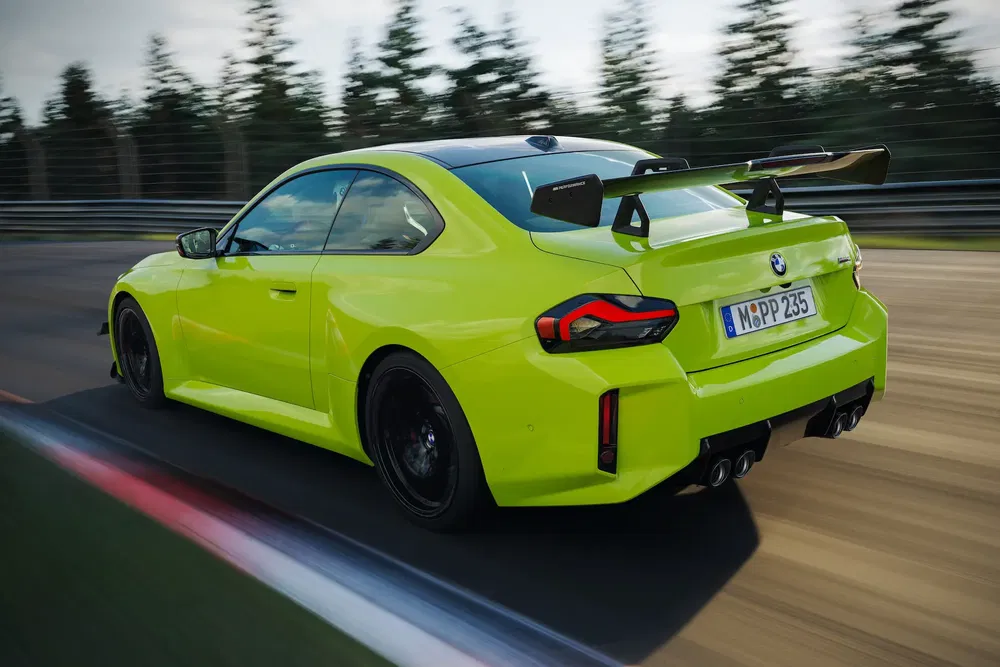 Felgroene BMW M2 op circuit, met opvallende achtervleugel, rijdend op hoge snelheid.