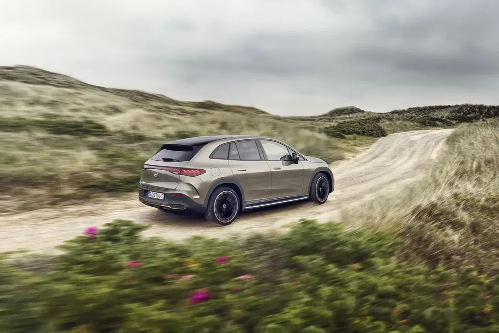 Elektrische Mercedes-Benz SUV rijdt op kronkelige, grasrijke landelijke weg.