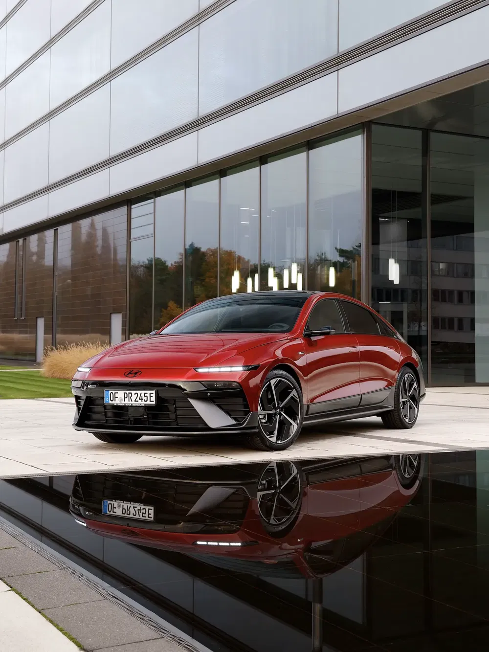 Hyundai Ioniq 6 rouge garée devant un immeuble moderne, reflet dans une flaque d'eau.