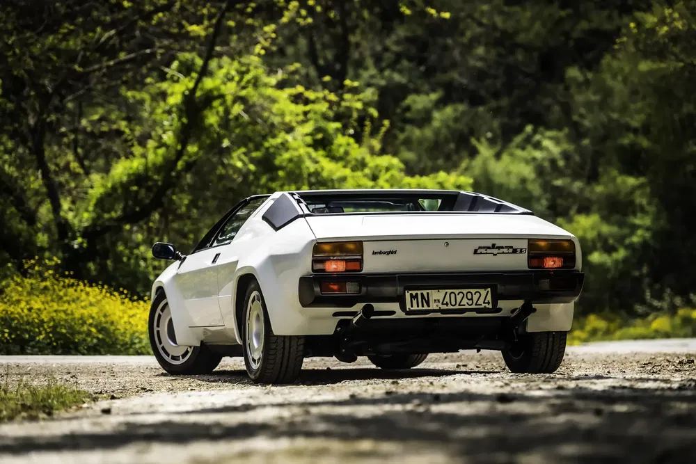 Lamborghini Jalpa blanc sur route de campagne, arrière ensoleillé, forêt en arrière-plan.