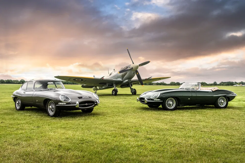 Twee Jaguar E-Type voor een vintage vliegtuig op een vliegveld bij zonsondergang.