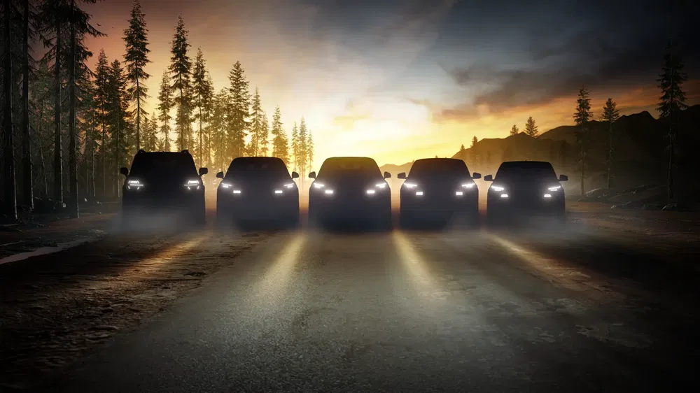{"fr":"Silhouettes de SUV alignés, phare allumés dans un paysage forestier au crépuscule.","nl":"Silhouetten van SUV's met koplampen aan in een boslandschap bij zonsondergang."}
