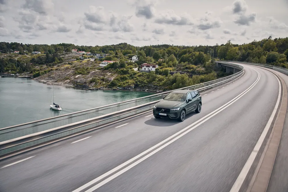 Volvo XC90 traverse un pont panoramique près d'une côte pittoresque, entourée de nature verdoyante.