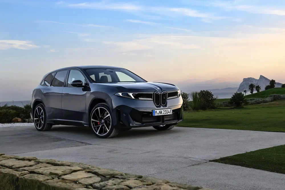 SUV BMW iX garé sur une allée, arrière-plan de coucher de soleil et colline verdoyante.