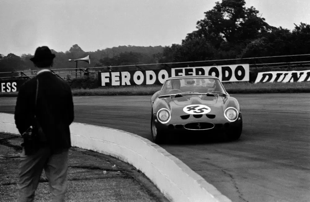 Ferrari 250 GTO en course vintage avec spectateur et panneaux publicitaires Ferodo.