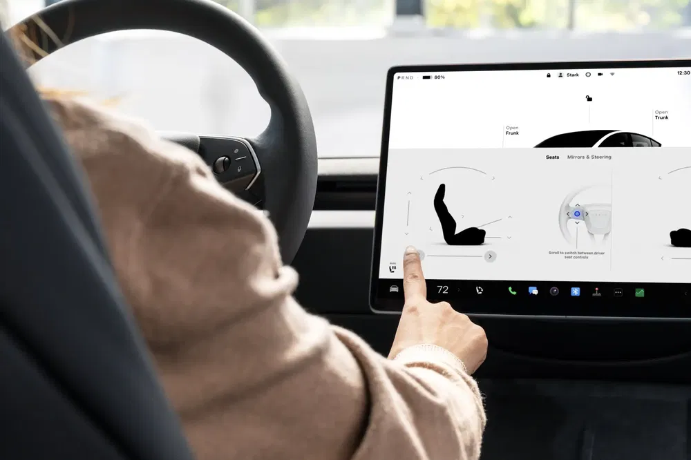 Conducteur interagissant avec l'écran tactile d'une Tesla, affichant les contrôles de siège.