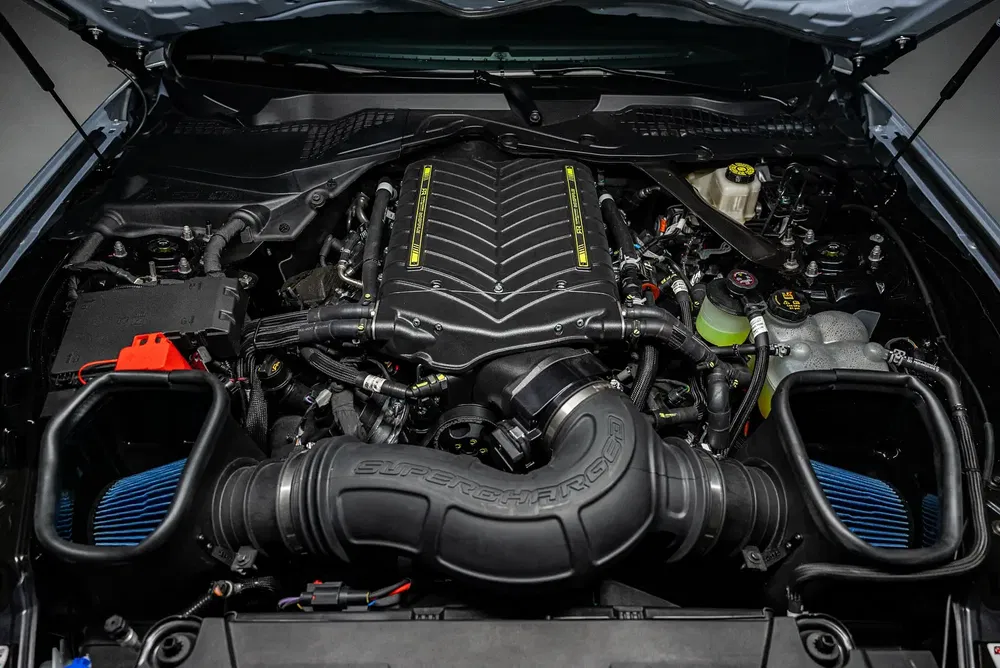 Moteur Ford Mustang 5.2L superchargé, capot ouvert, avec composants noirs et détails jaunes.