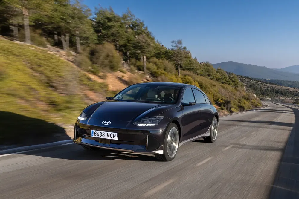 Hyundai Ioniq 6 noir sur route de montagne, ciel dégagé et nature luxuriante.