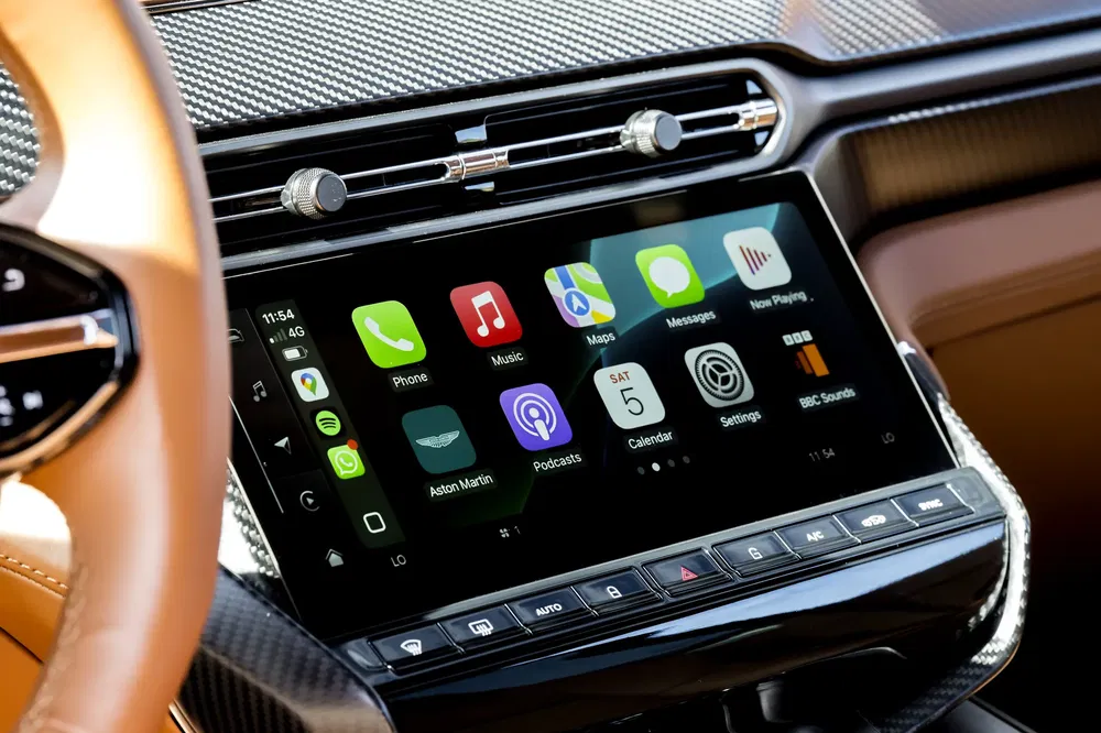 Intérieur de l'Aston Martin avec écran multimédia affichant Apple CarPlay et applications diverses.