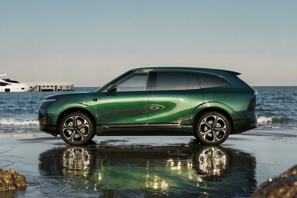 SUV vert Aiways U6 garé sur la plage avec reflet sur l'eau.