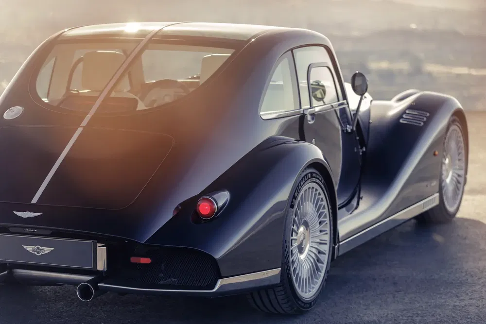 Vue arrière d'une Morgan Aero 8 noire au coucher de soleil sur une route dégagée.