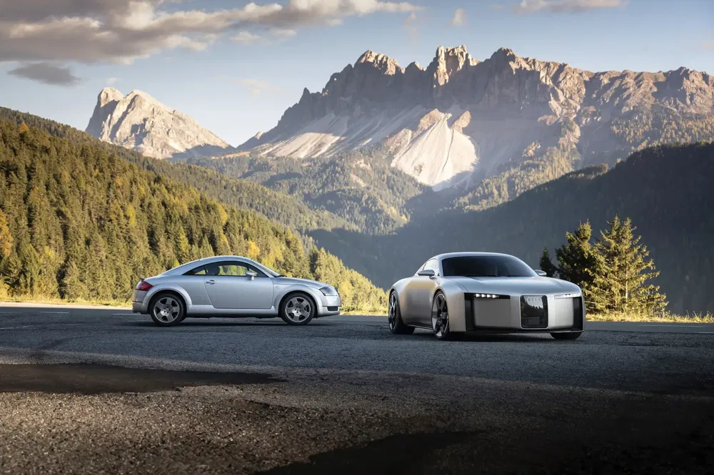 Deux voitures sportives argentées, Audi TT et concept futuriste, devant montagnes majestueuses.