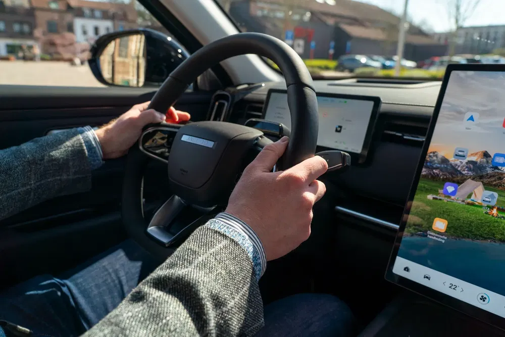 Bestuurder in een moderne auto met touchscreen en gevormd stuur.