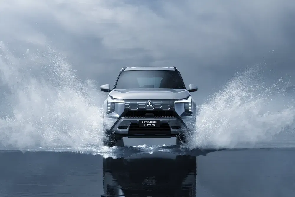 Mitsubishi Outlander traverse une flaque d'eau avec éclaboussures dynamiques, ciel orageux en arrière-plan.