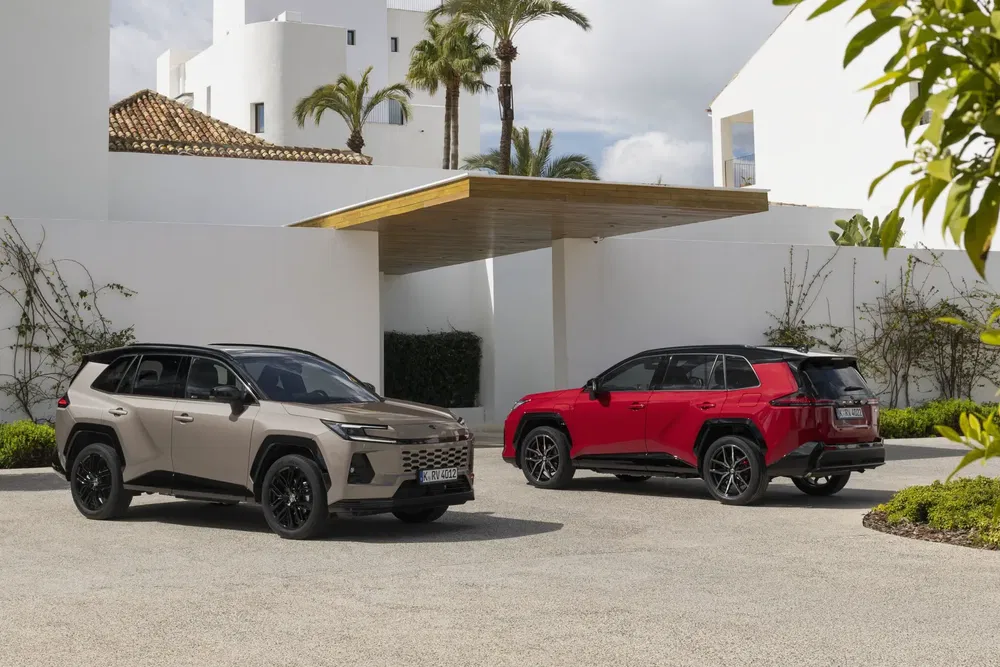 Twee moderne Toyota RAV4's geparkeerd voor een eigentijds huis met palmbomen op de achtergrond.