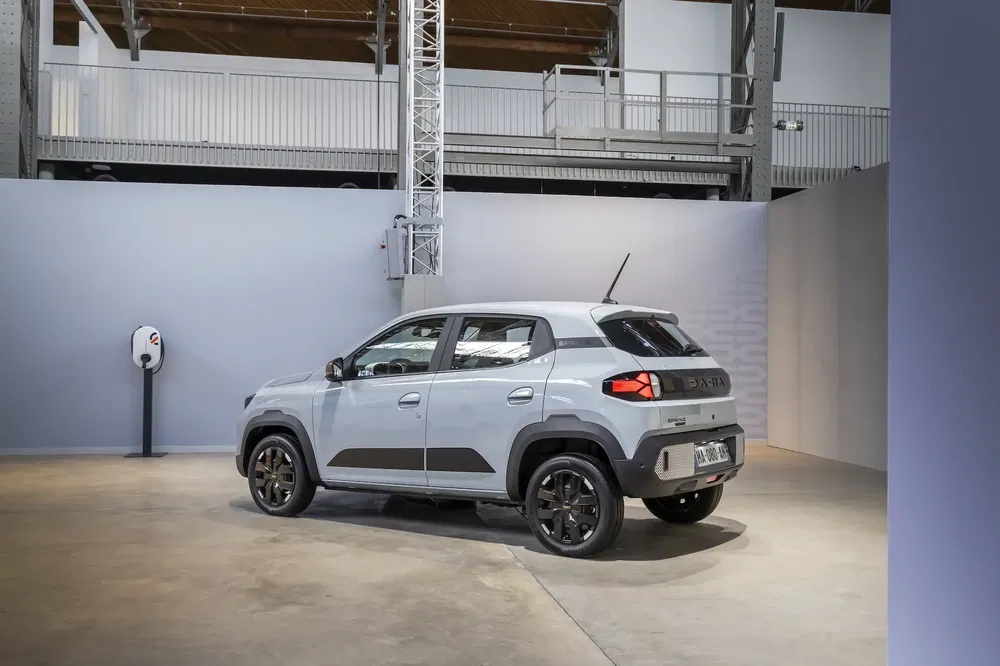 Grijze elektrische Dacia Spring in een moderne garage, zij-achteraanzicht.