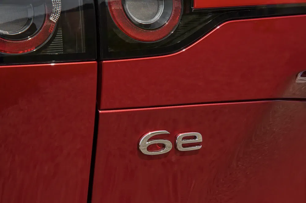 Detail van de badge aan de achterkant van een rode auto met '6e' en achterlichten zichtbaar.