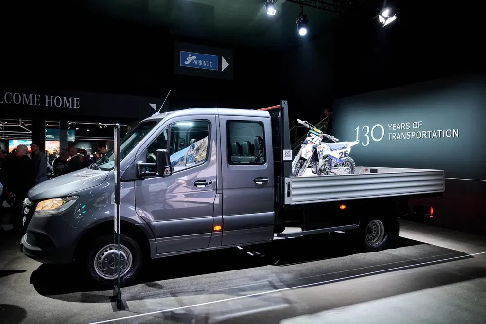 Camion Mercedes-Benz Sprinter avec moto tout-terrain exposée lors d'un événement automobile.