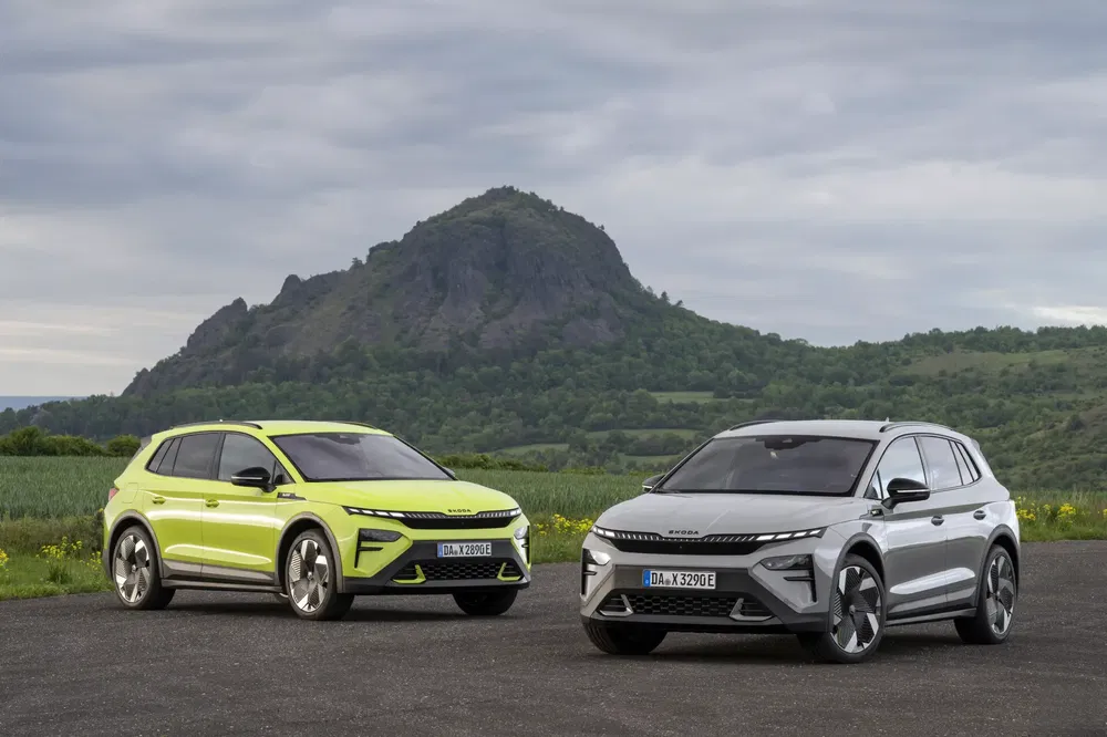 Twee elektrische Skoda Enyaq iV's voor een groene berg, bewolkte lucht.