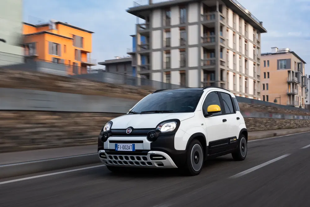{"fr":"Fiat Panda blanche en mouvement sur une route urbaine avec bâtiments modernes en arrière-plan.","nl":"Witte Fiat Panda rijdend op stedelijke weg met moderne gebouwen op de achtergrond."}