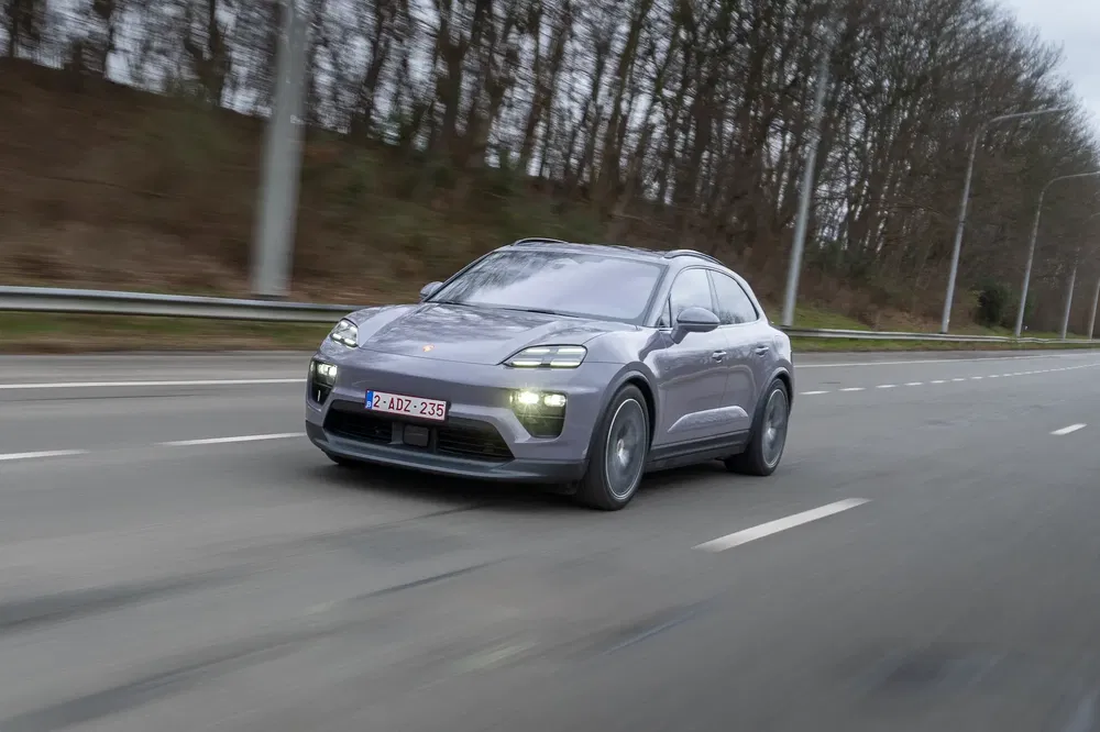 Porsche Macan gris roulant sur une autoroute bordée d'arbres en hiver.