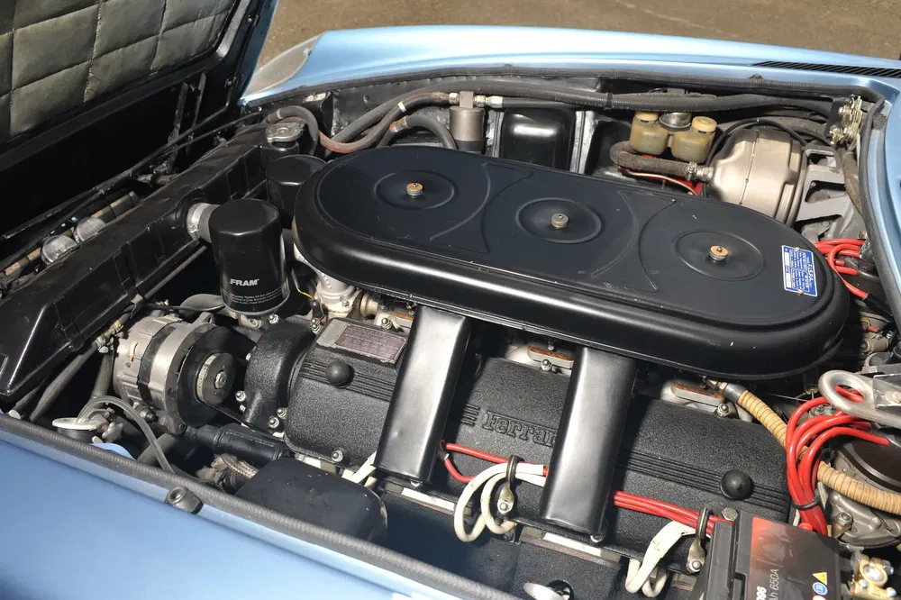 Klassieke Ferrari-motor met zichtbare onderdelen, rode kabels en kenmerkend zwart luchtfilter.