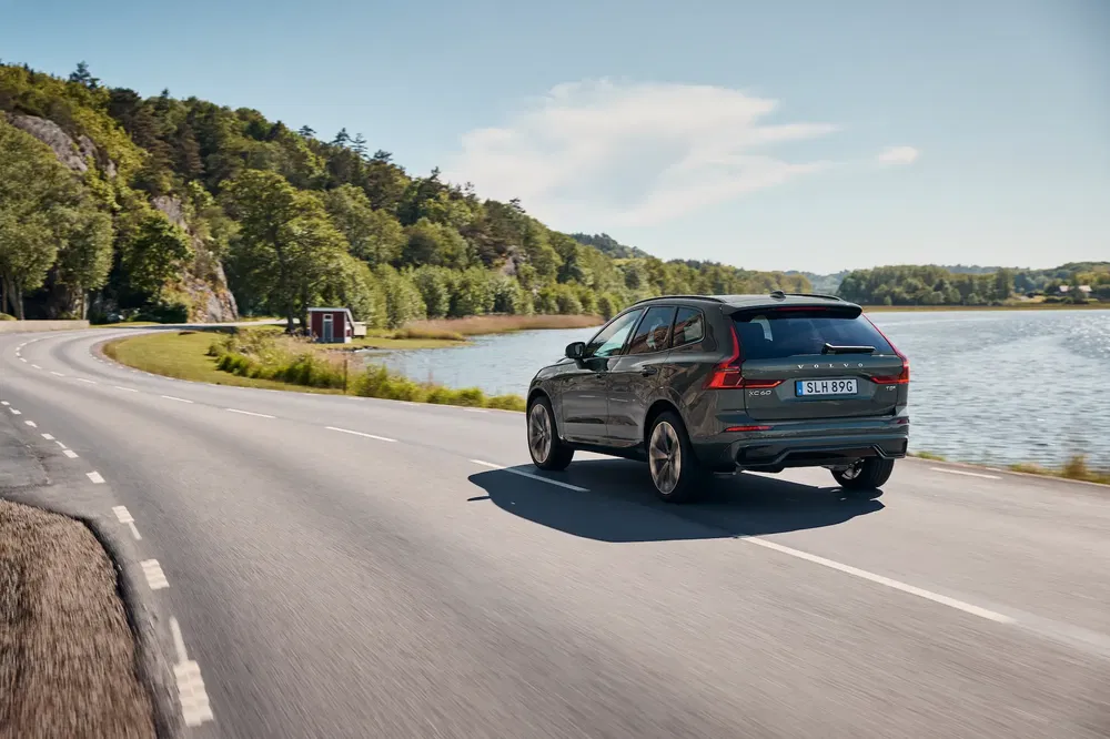 Volvo XC60 sur route côtière ensoleillée avec paysage verdoyant et lac.