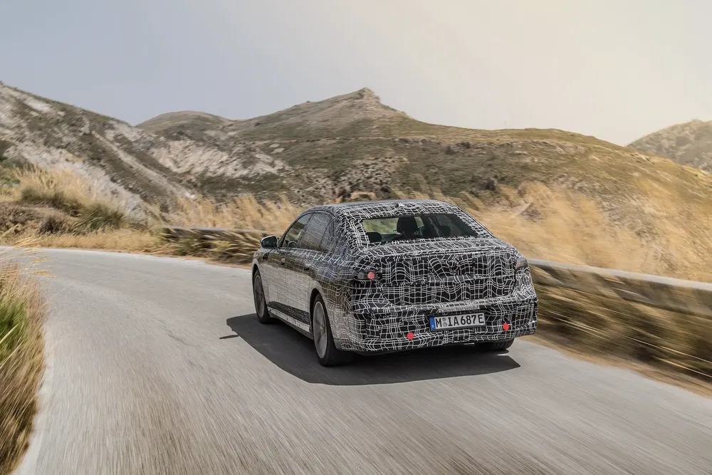 Prototype BMW camouflage sur route de montagne sinueuse au coucher du soleil.