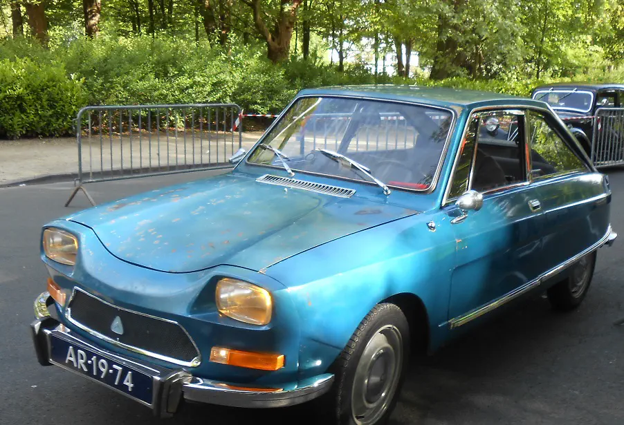Voiture vintage bleu Panhard CD sur route entourée de barrières et arbres verdoyants.