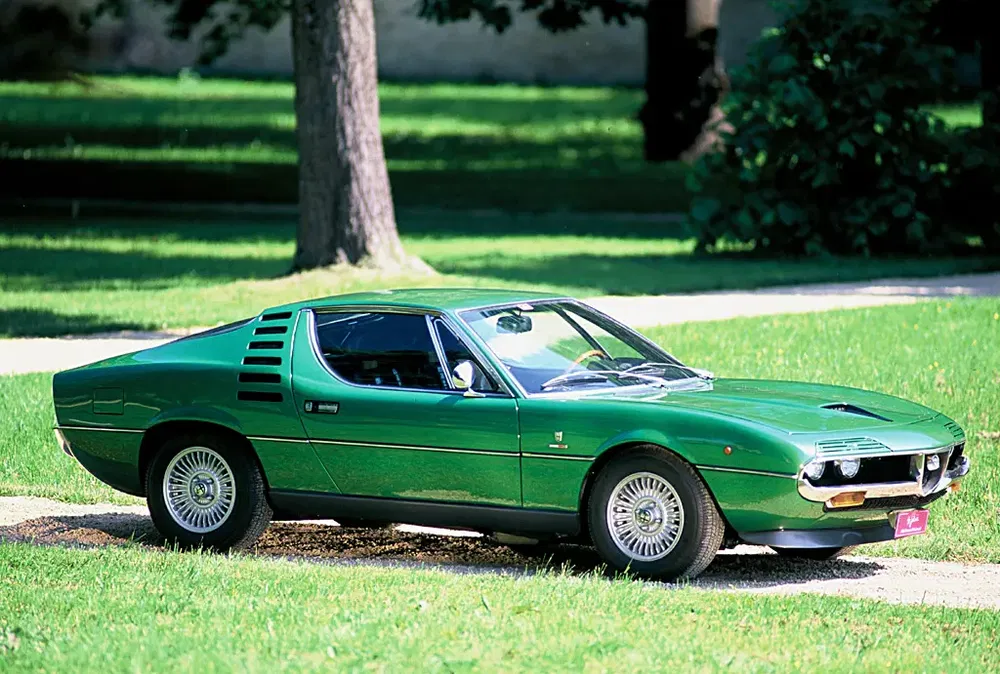 Alfa Romeo Montreal verte stationnée dans un parc verdoyant, design classique des années 70.