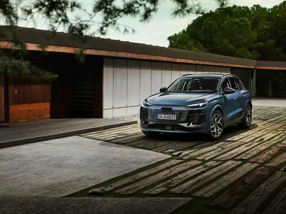 Audi Q4 e-tron geparkeerd voor een modern houten en betonnen huis.