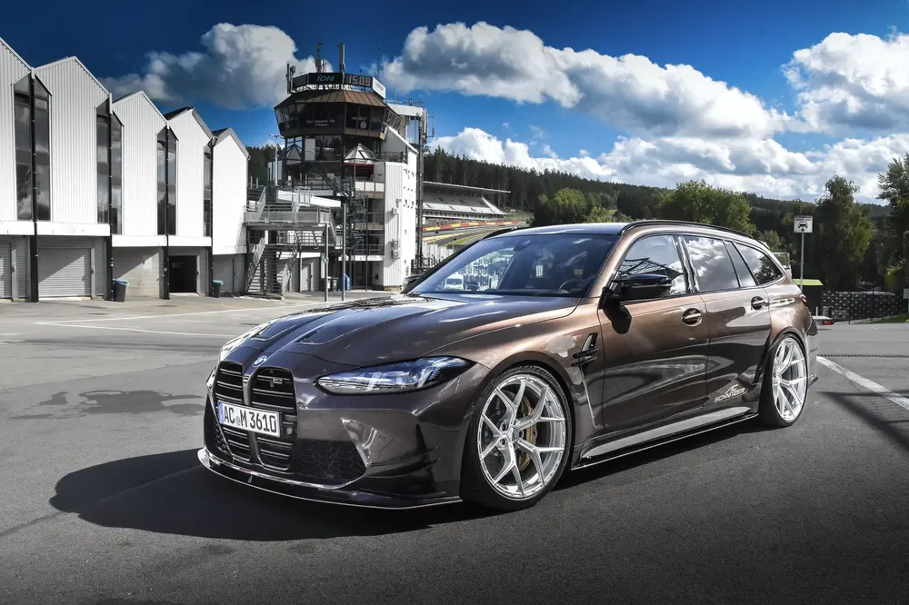 BMW break marron sur piste avec arrière-plan de bâtiment moderne et ciel nuageux.