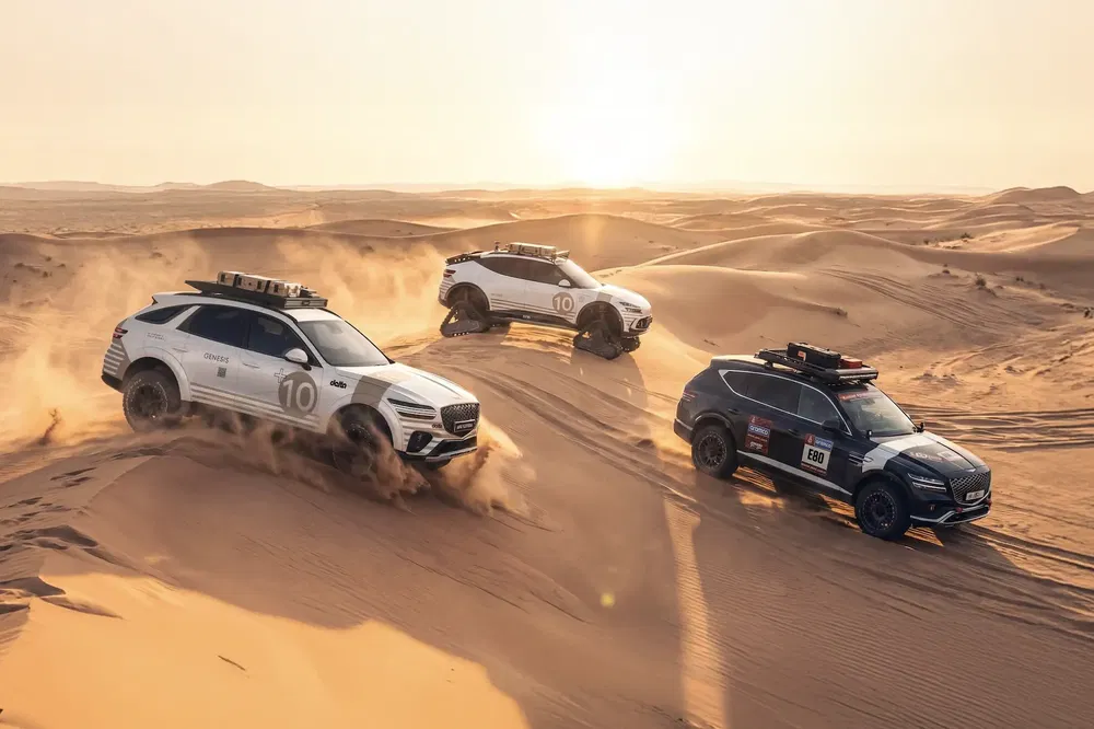 Trois SUV Genesis GV80 défiant les dunes de sable d'un désert au coucher du soleil.