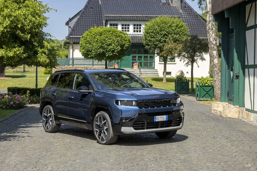 SUV moderne Jeep Compass stationné devant une maison traditionnelle en briques avec jardin soigné.