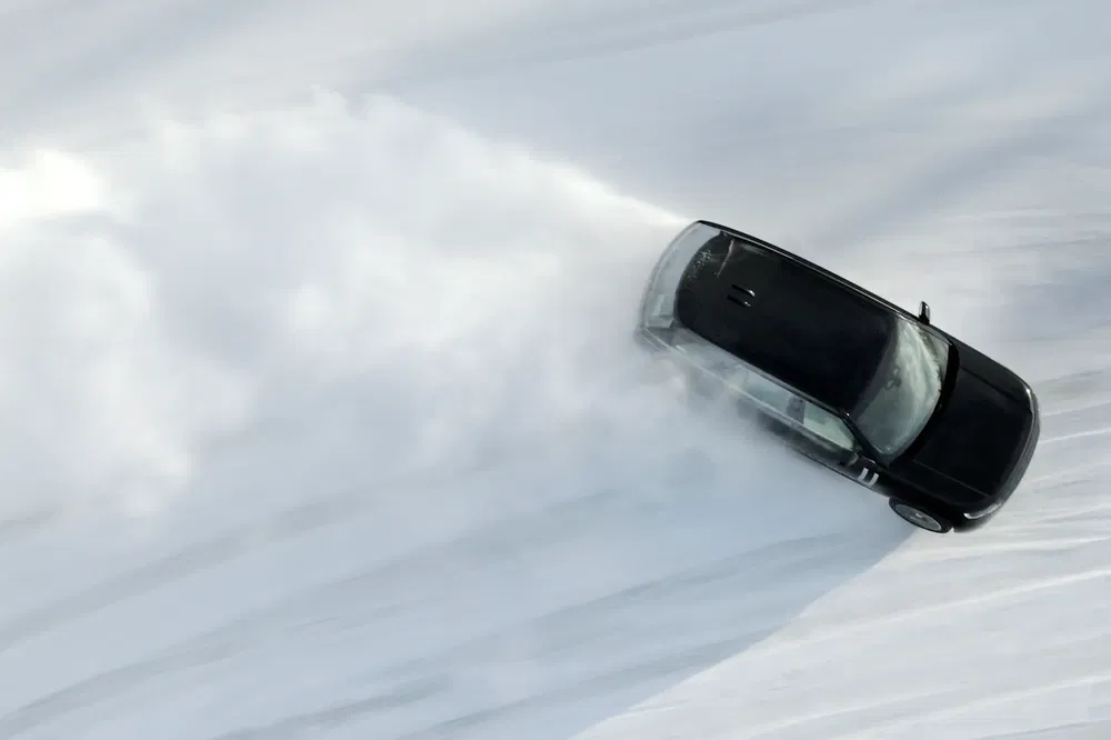 Zwarte auto drijft over sneeuw, vormt spectaculaire sneeuwwolk.