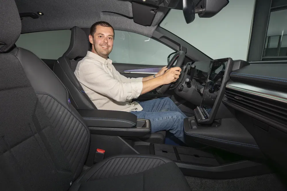 Conducteur souriant dans l'habitacle moderne d'une voiture, avec tableau de bord numérique.