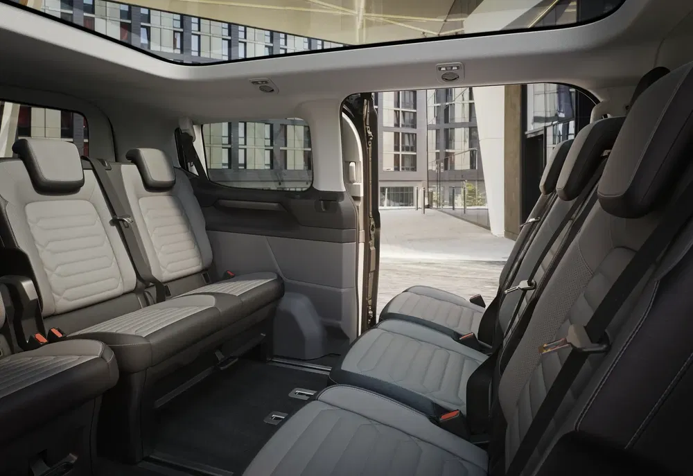 Intérieur spacieux d'un fourgon moderne avec sièges confortables et porte coulissante ouverte.