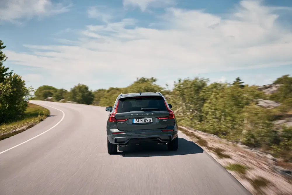 Volvo XC60 T8 roulant sur une route sinueuse entourée de verdure et ciel bleu.