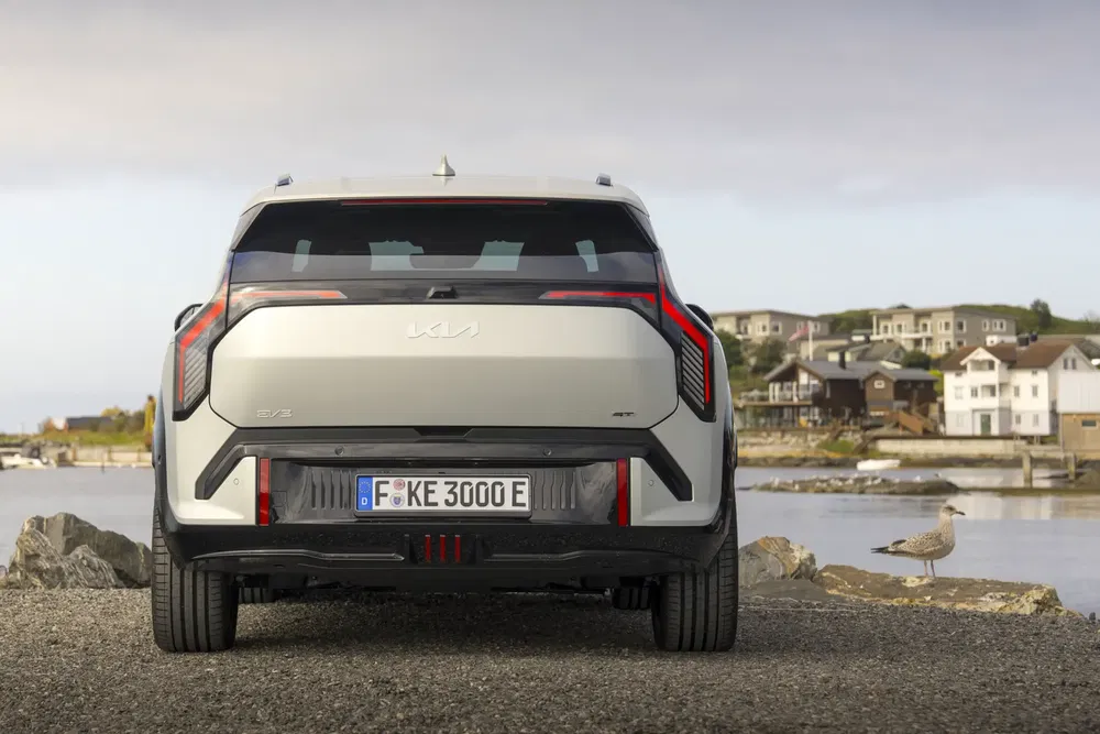 Arrière du Kia EV9 stationné près d'un lac avec vue sur des maisons.
