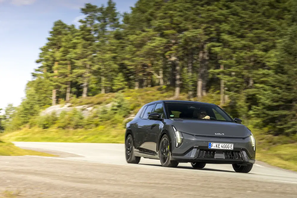 Kia EV6 noire sur route de campagne bordée d'arbres, ciel dégagé en arrière-plan.