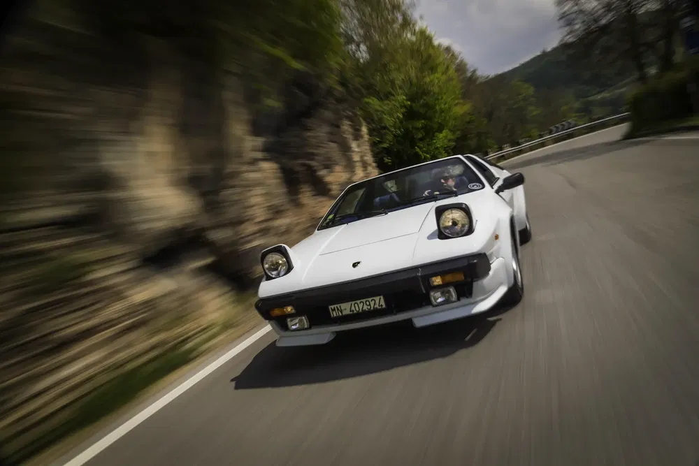 Lamborghini Jalpa blanche roulant à grande vitesse sur une route sinueuse de campagne.