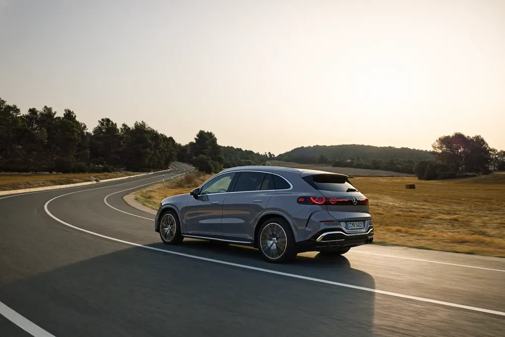 Grijze Mercedes-Benz EQE SUV op kronkelige weg bij schemering, moderne elektrische auto's.