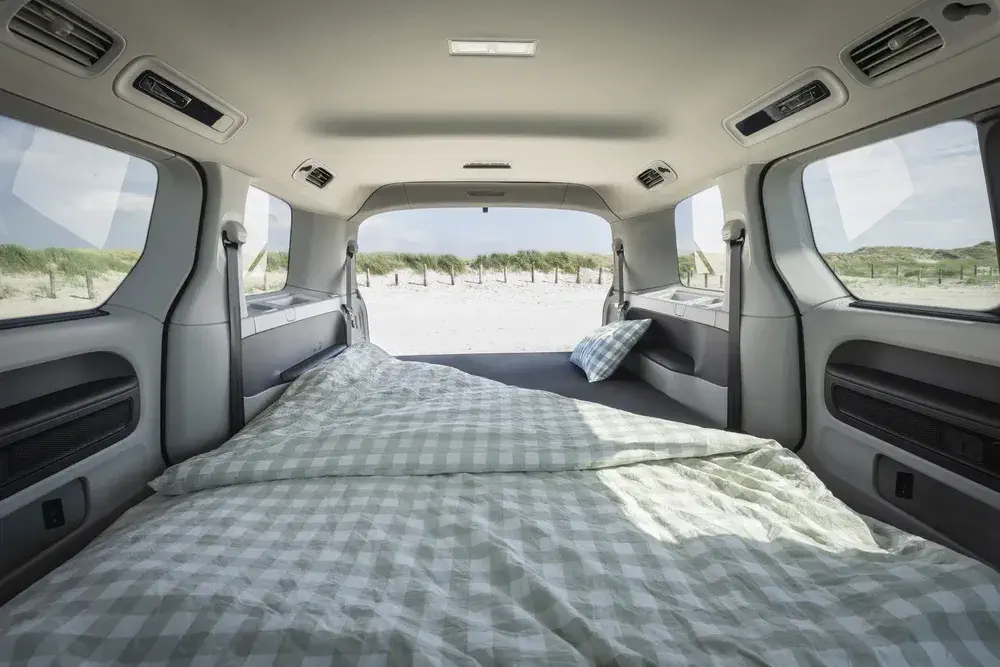 Intérieur d'un van aménagé avec un lit à l'arrière, vue sur la plage.