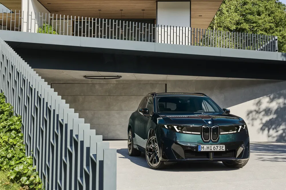 BMW iX vert garé devant une maison moderne avec architecture contemporaine.